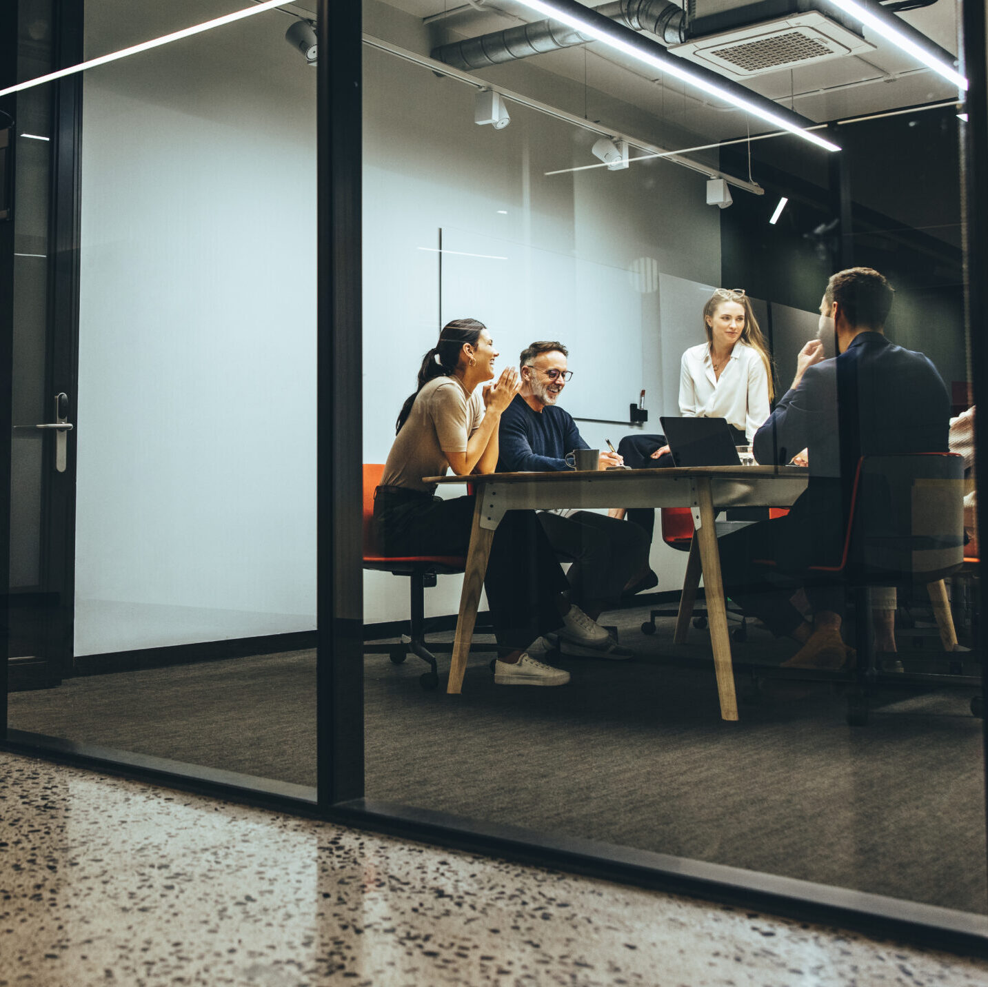 Business colleagues having a meeting in a transparent boardroom. Group of happy business professionals having a discussion during a briefing. Diverse businesspeople collaborating on a new project.